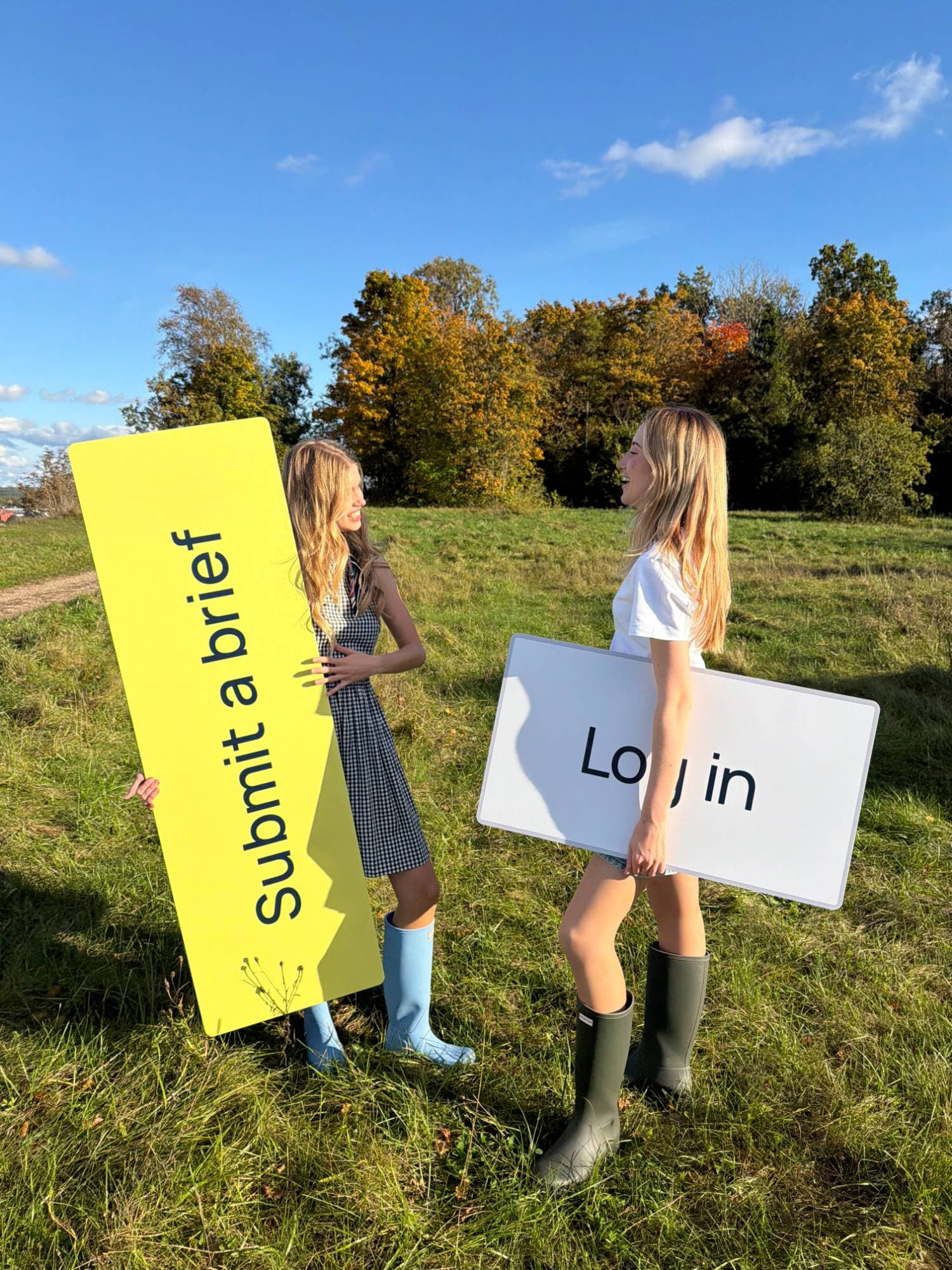 Hannah and Lotta in a field holding giant 'Submit a brief' and 'Log in' buttons